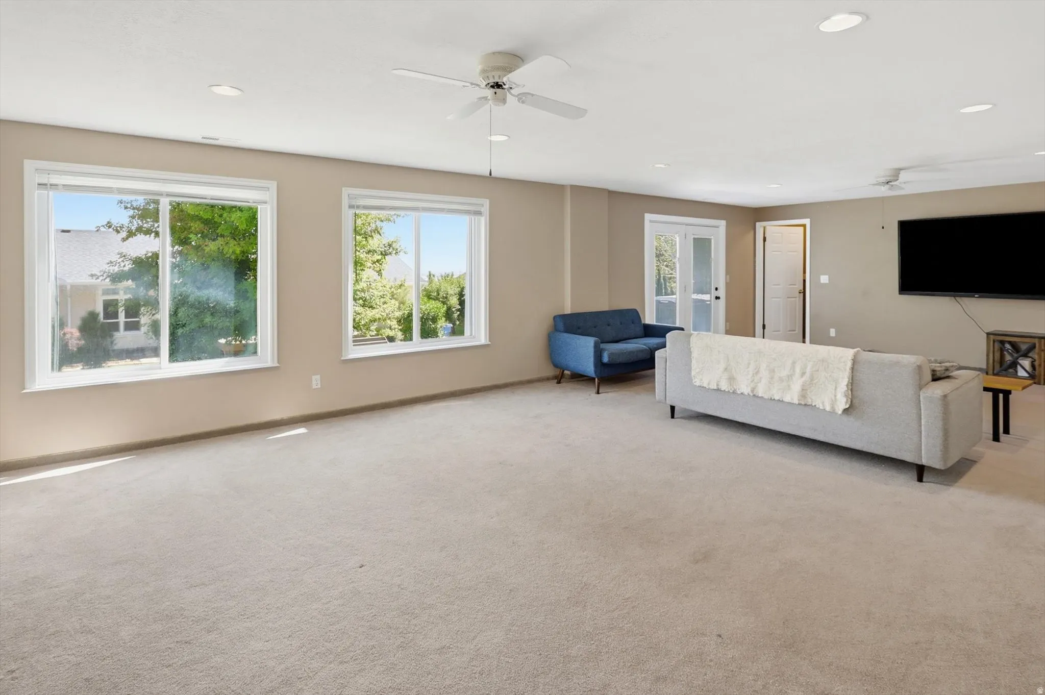 Spacious room featuring light tan walls, two large windows, recessed ceiling lighting, and two ceiling fans