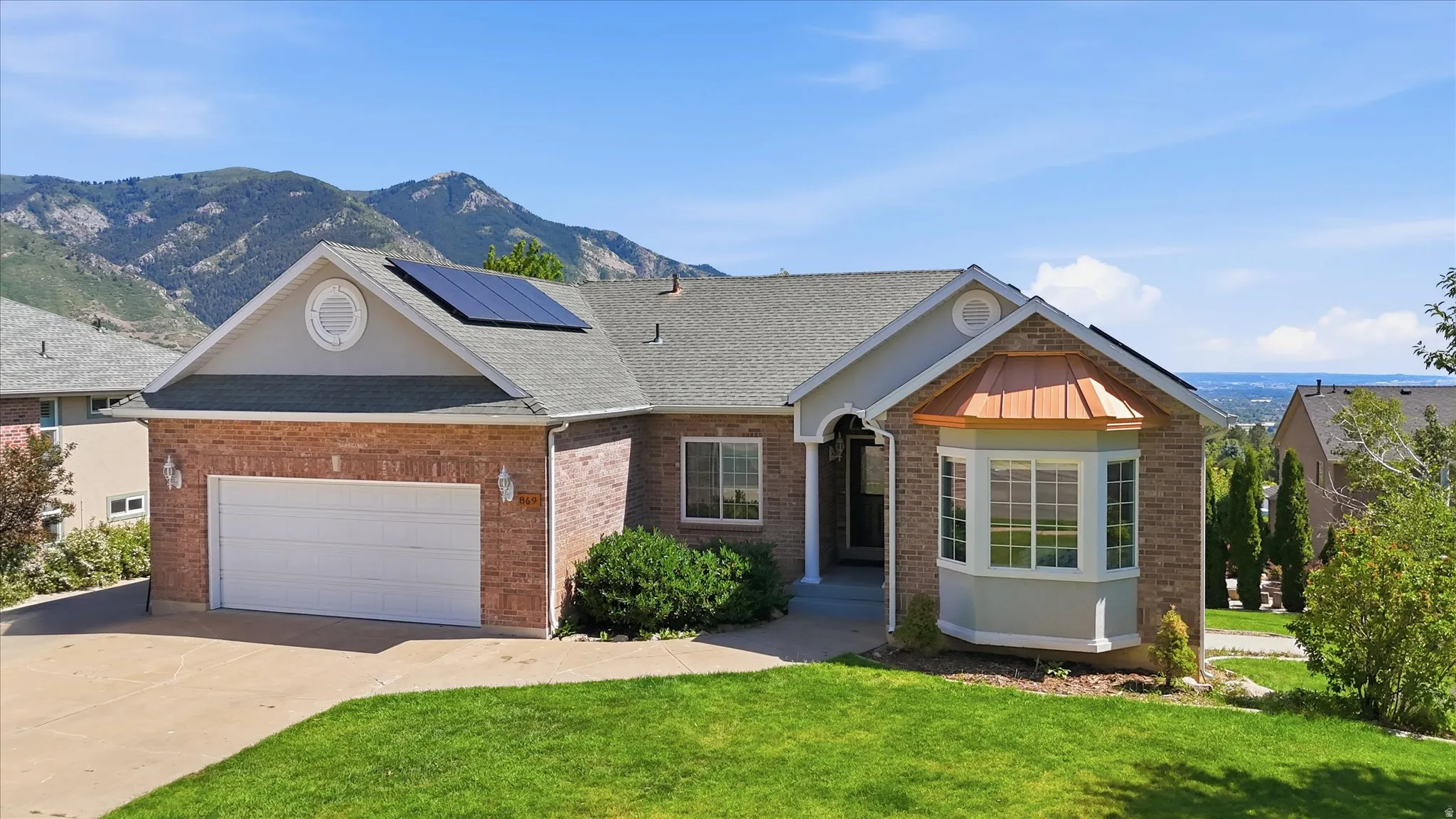 Brick-clad exterior featuring a two-car garage, solar panels, and a prominent bay window with a copper-tone roof accent