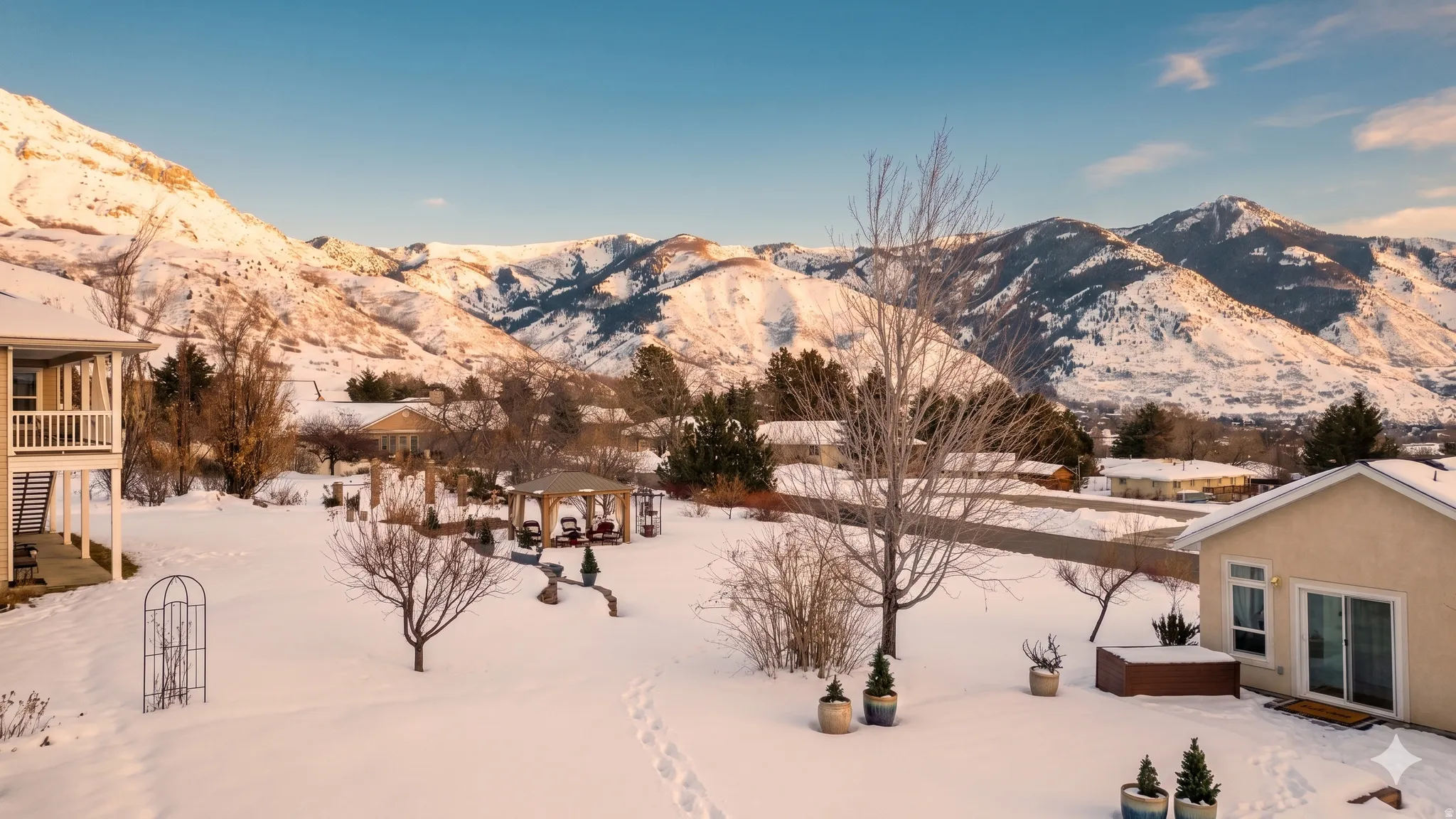 Expansive backyard featuring a covered gazebo, hot tub, and mature trees against a backdrop of snow-capped mountains