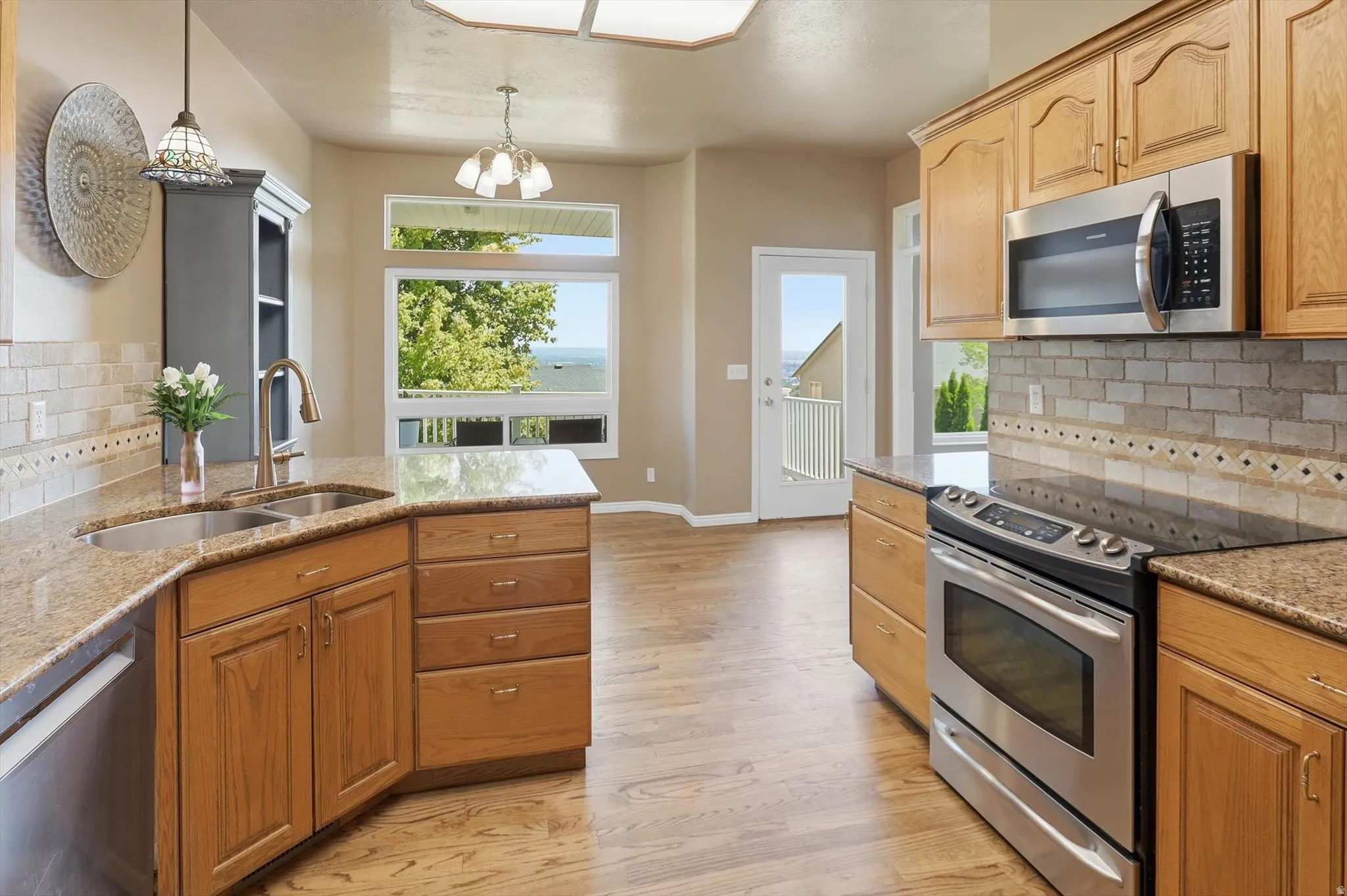 Kitchen featuring light wood-finish cabinetry, stainless steel appliances, granite countertops, and a subway tile backsplash