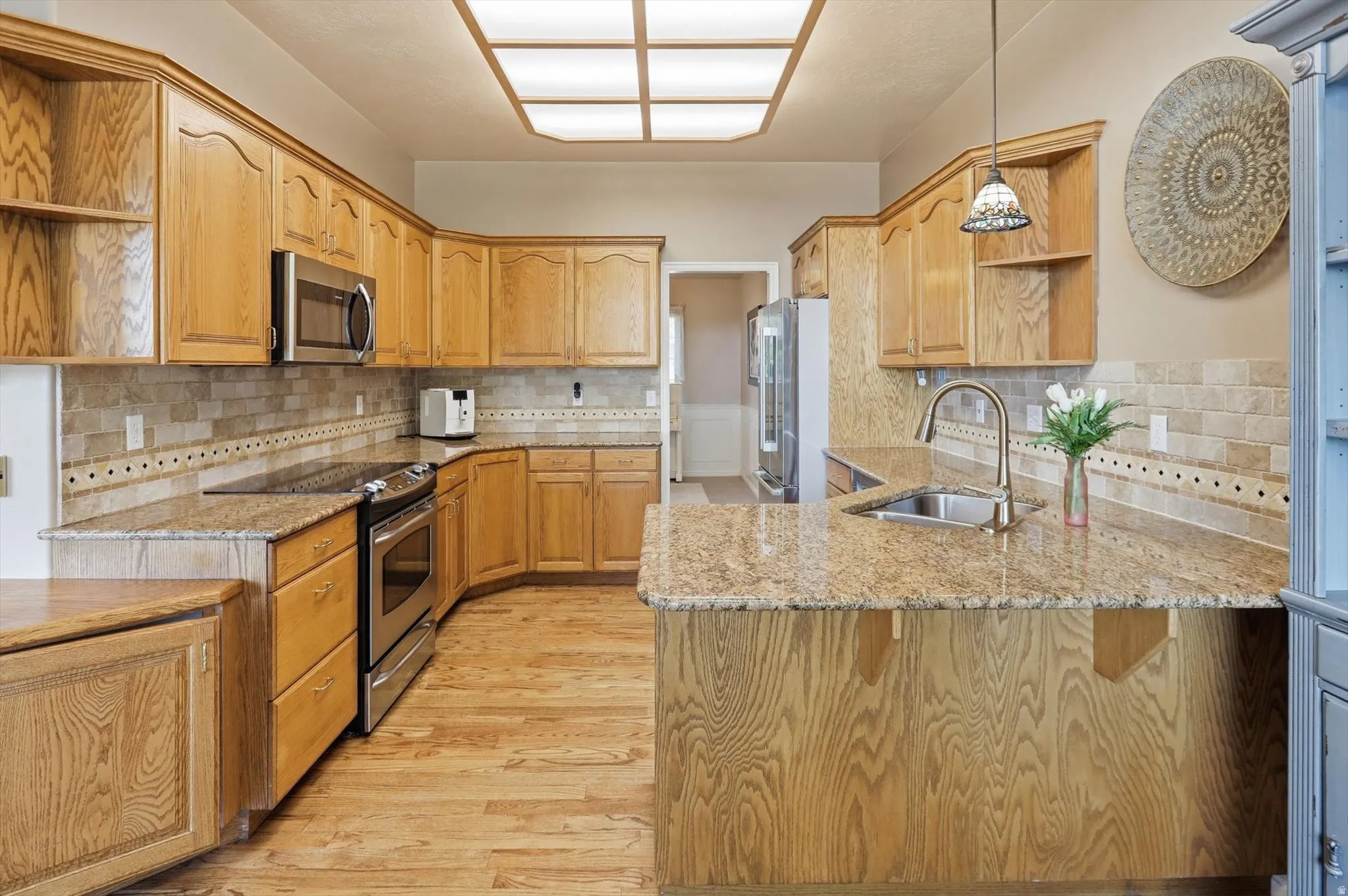 Kitchen featuring extensive wood cabinetry, granite countertops, stainless steel appliances, tile backsplash, and wood-finish flooring