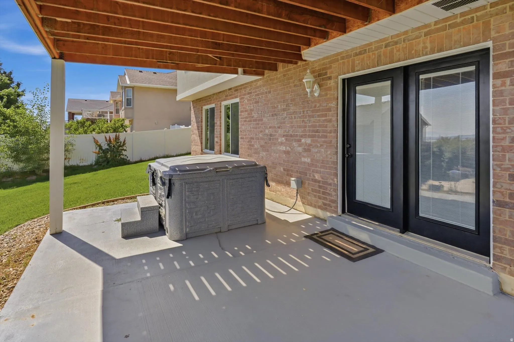 Covered concrete patio with a hot tub and manicured lawn
