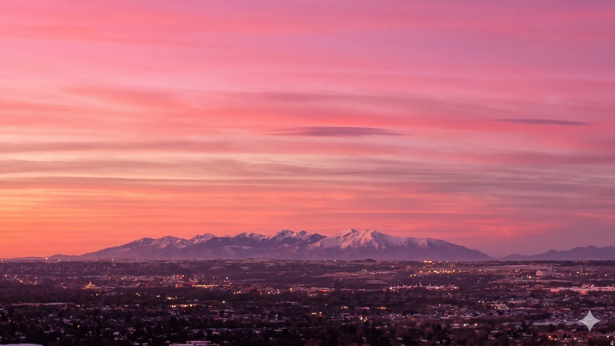 Panoramic cityscape with distant snow-capped mountains under a vibrant, multi-hued sky