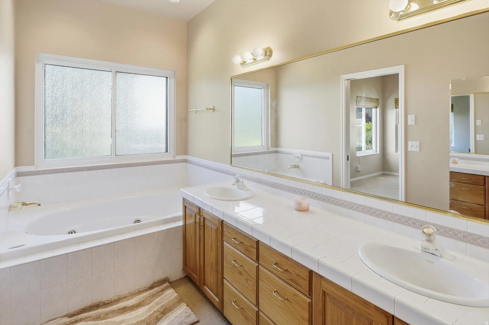 Double vanity with white tile countertop, dual integrated sinks, and ample wood cabinetry