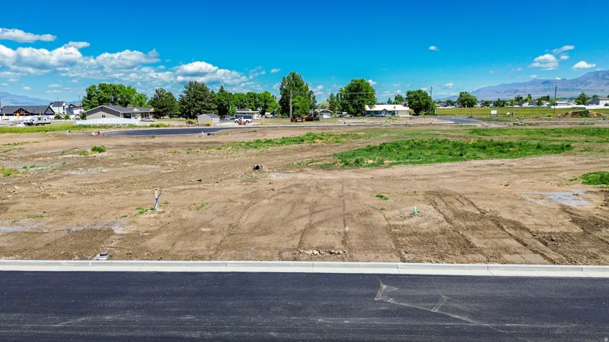 Graded dirt parcel with paved road frontage, curb, and distant mountain backdrop
