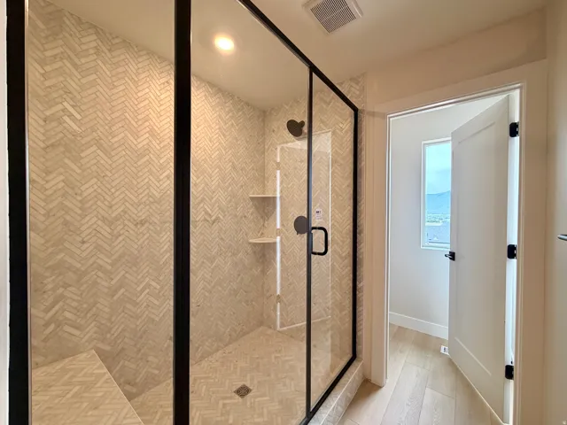 Walk-in shower with black-framed glass enclosure, herringbone pattern wall and floor tile, built-in shower bench, and recessed shelving
