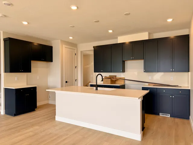 Contemporary kitchen featuring dark cabinetry, light countertops, a central island with an integrated sink, recessed lighting, and wood-finish flooring