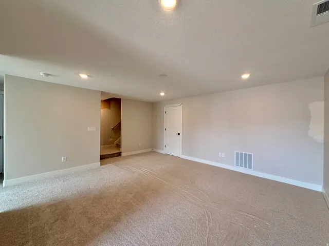 Spacious room featuring neutral carpeting, recessed lighting, a white interior door with black hardware, and light-toned walls