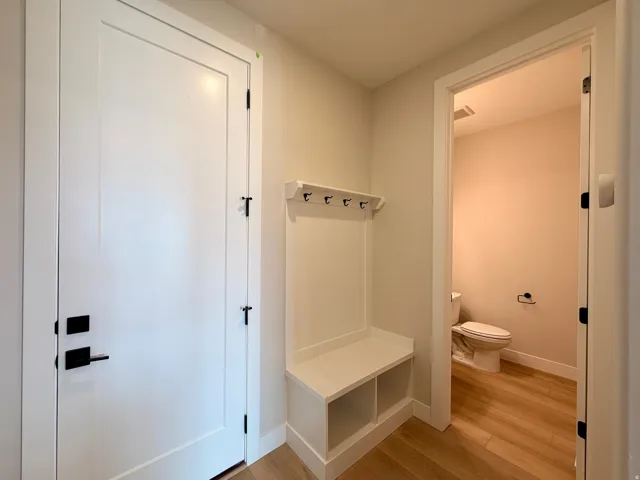 Entryway featuring a built-in bench with storage cubbies and coat hooks, modern white doors with matte black hardware, and wood-finish flooring