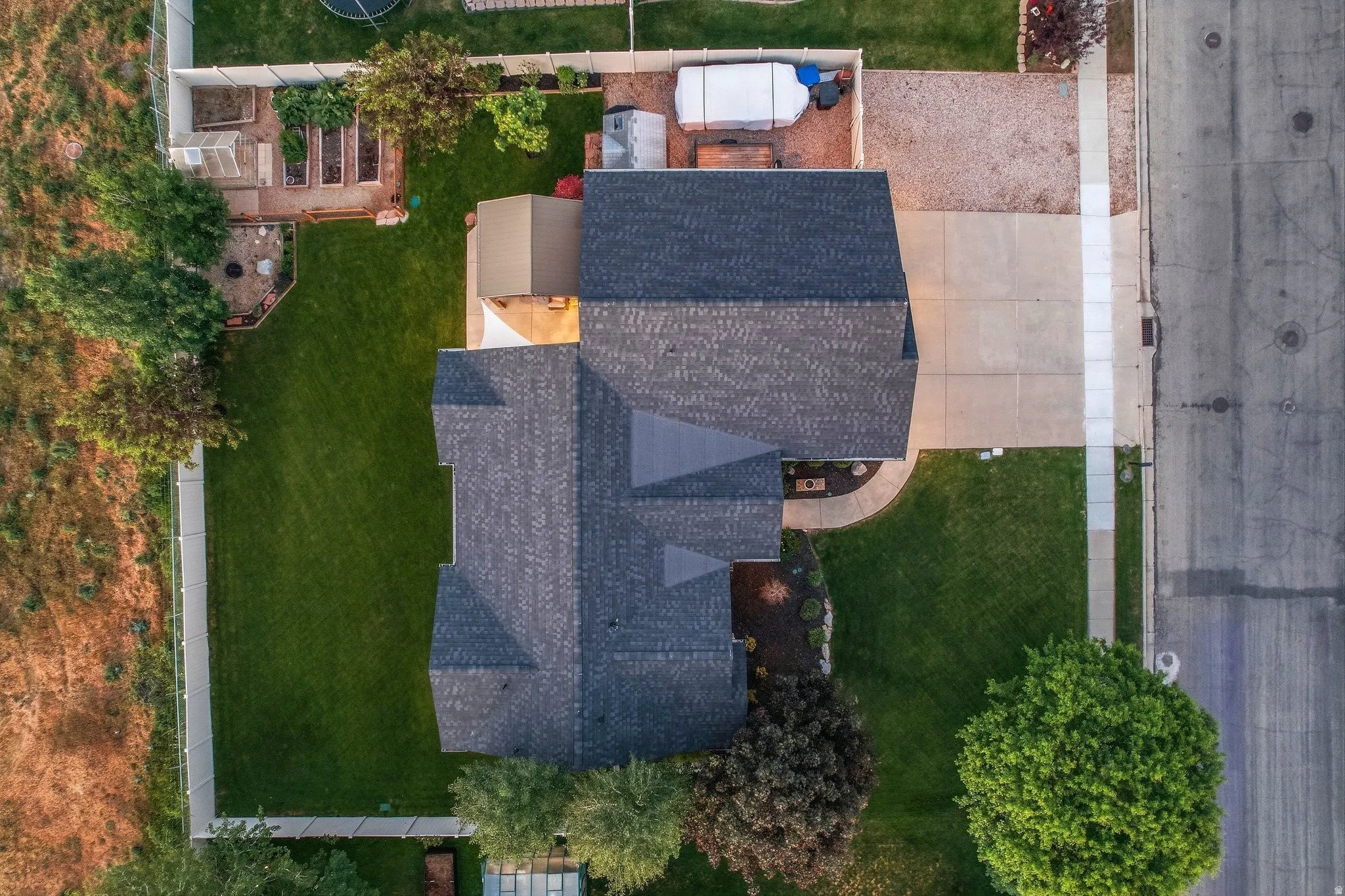 Aerial view of a residential property featuring a dark shingle roof, concrete driveway, and a manicured lawn