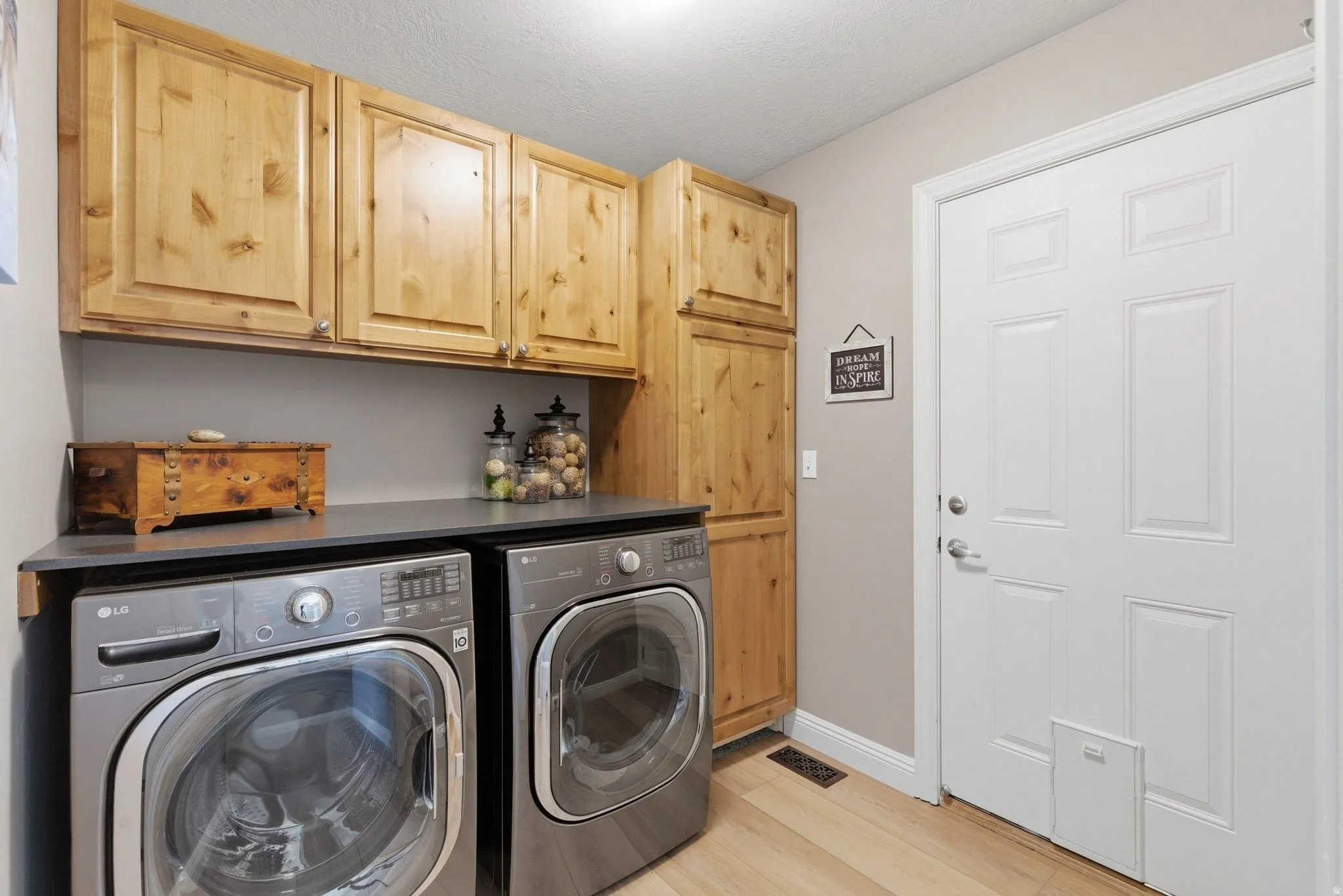 Laundry area featuring wood-finish cabinetry, a dark countertop, and light wood-finish flooring