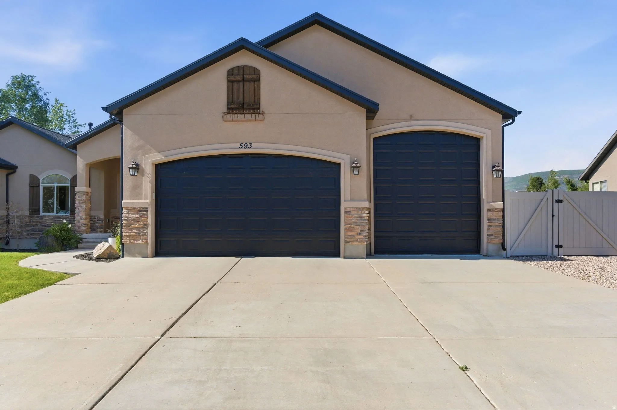 Stucco exterior featuring a two-car garage with arched entrances, stone accents, and decorative lighting fixtures