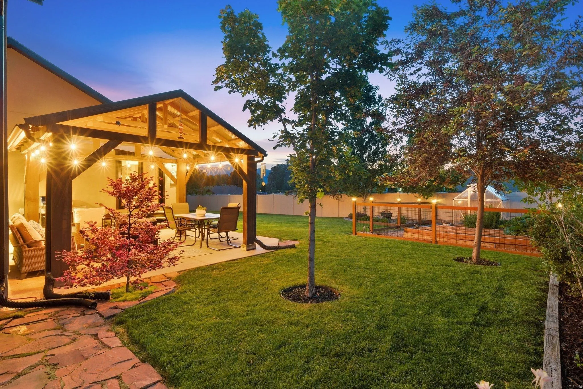 Expansive backyard featuring a covered patio with exposed wood beams, string lighting, and a stone paver path
