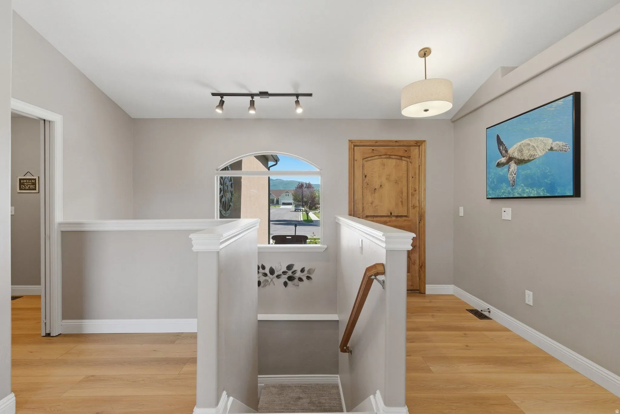 Upper-level landing featuring light wood-finish flooring, a white spindle-style railing, and an arched window
