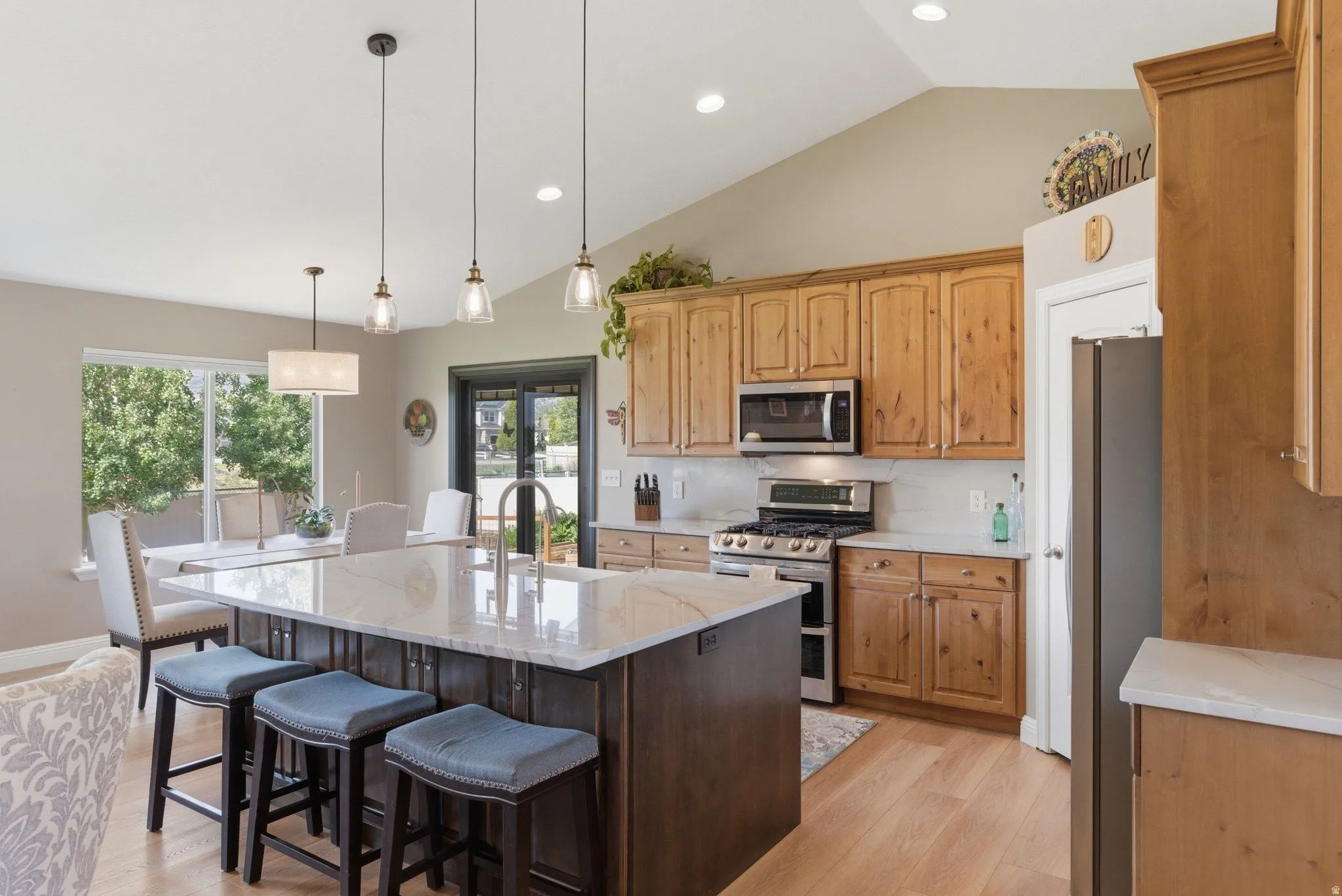 Spacious kitchen featuring a large island with a light-toned countertop, wood-finish flooring, recessed lighting, stainless steel appliances, and abundant natural wood cabinetry