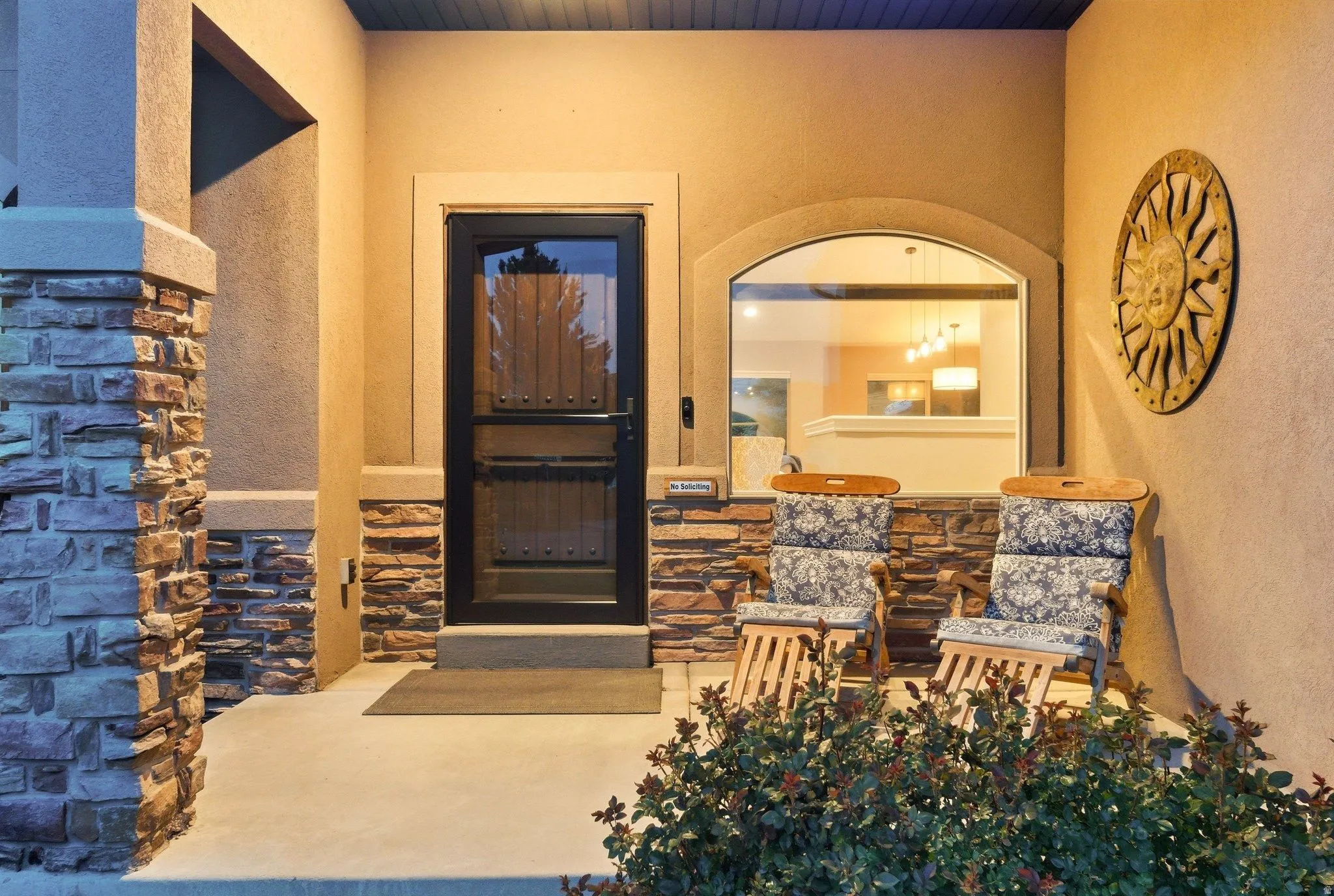 Covered front porch featuring a stone veneer accent wall, stucco exterior, and concrete flooring
