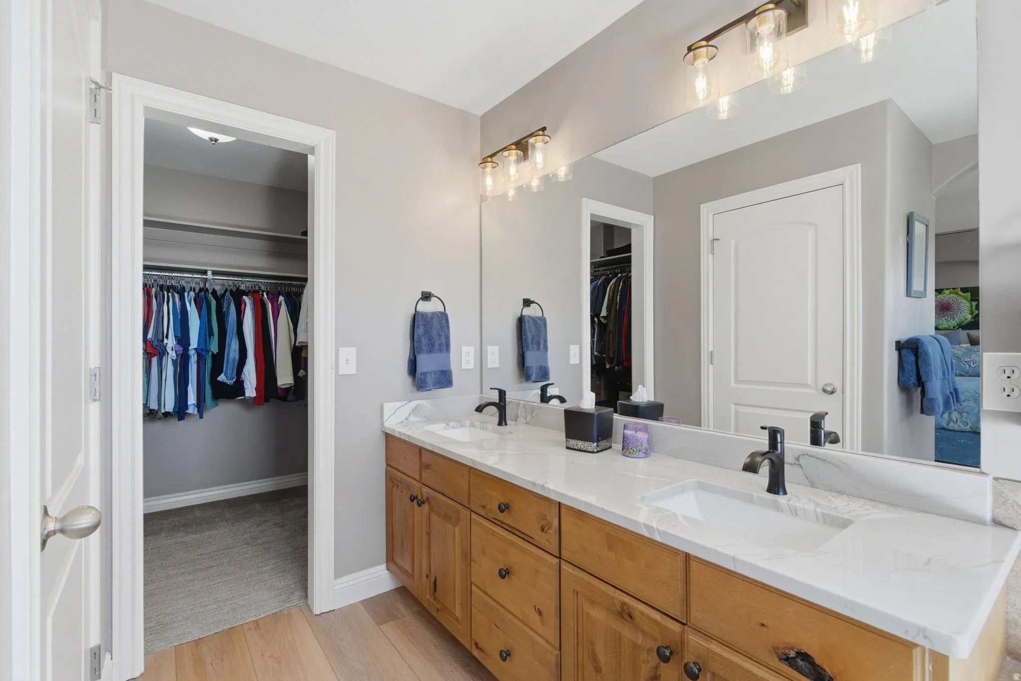 Double vanity featuring natural wood cabinetry, white stone countertops, dual integrated sinks, and matte black fixtures