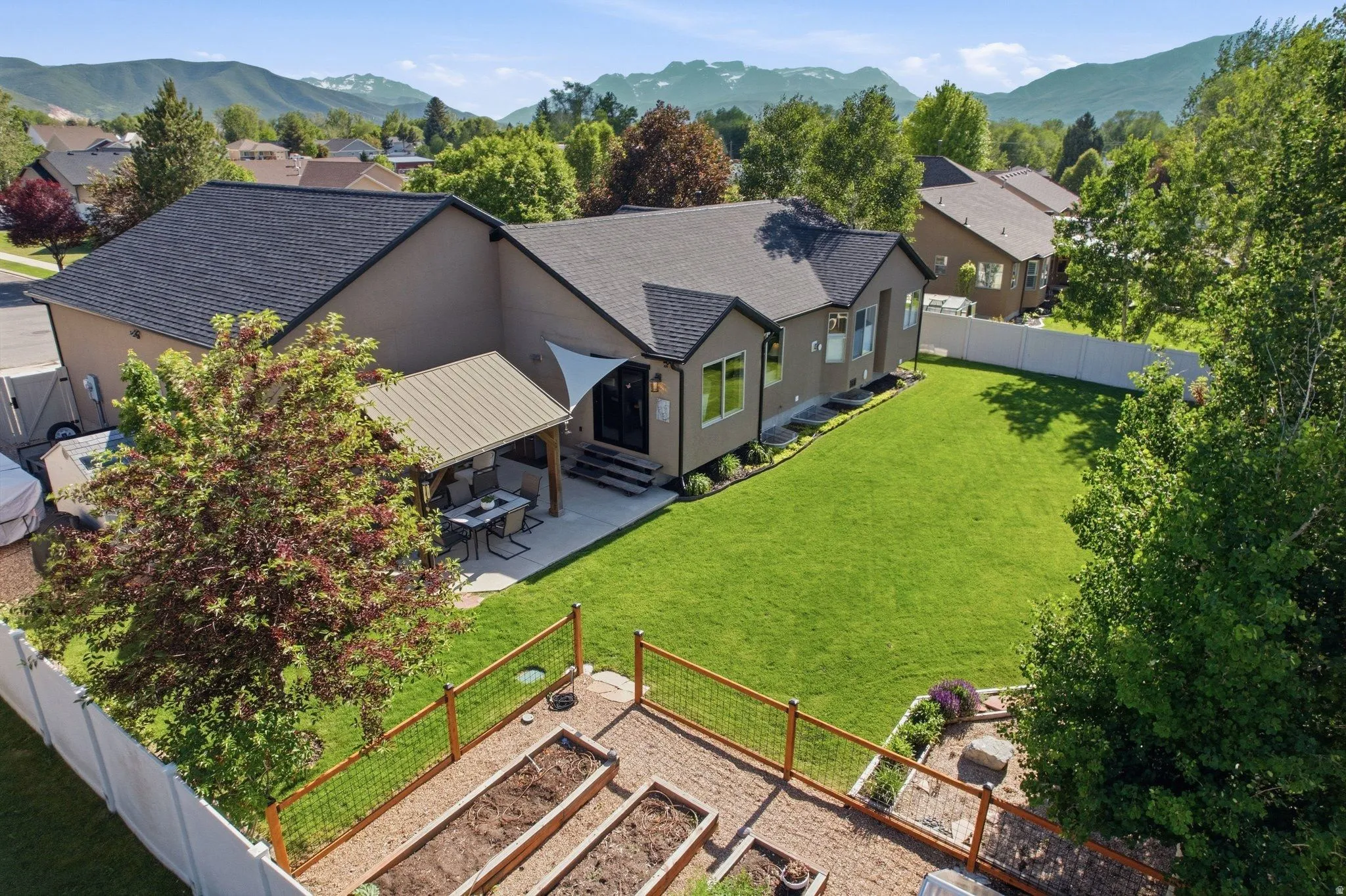 Rear exterior featuring a covered patio, expansive lawn, raised garden beds, and mountain scenery