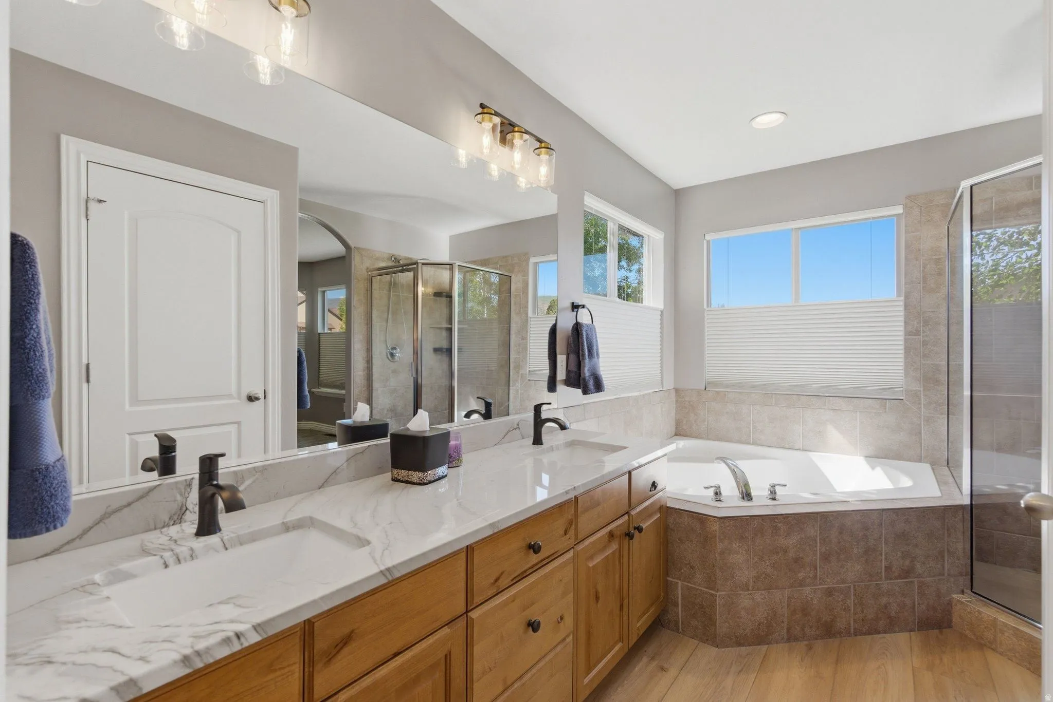 Bathroom featuring a dual vanity with a marbled countertop, light wood-finish cabinetry, and black fixtures