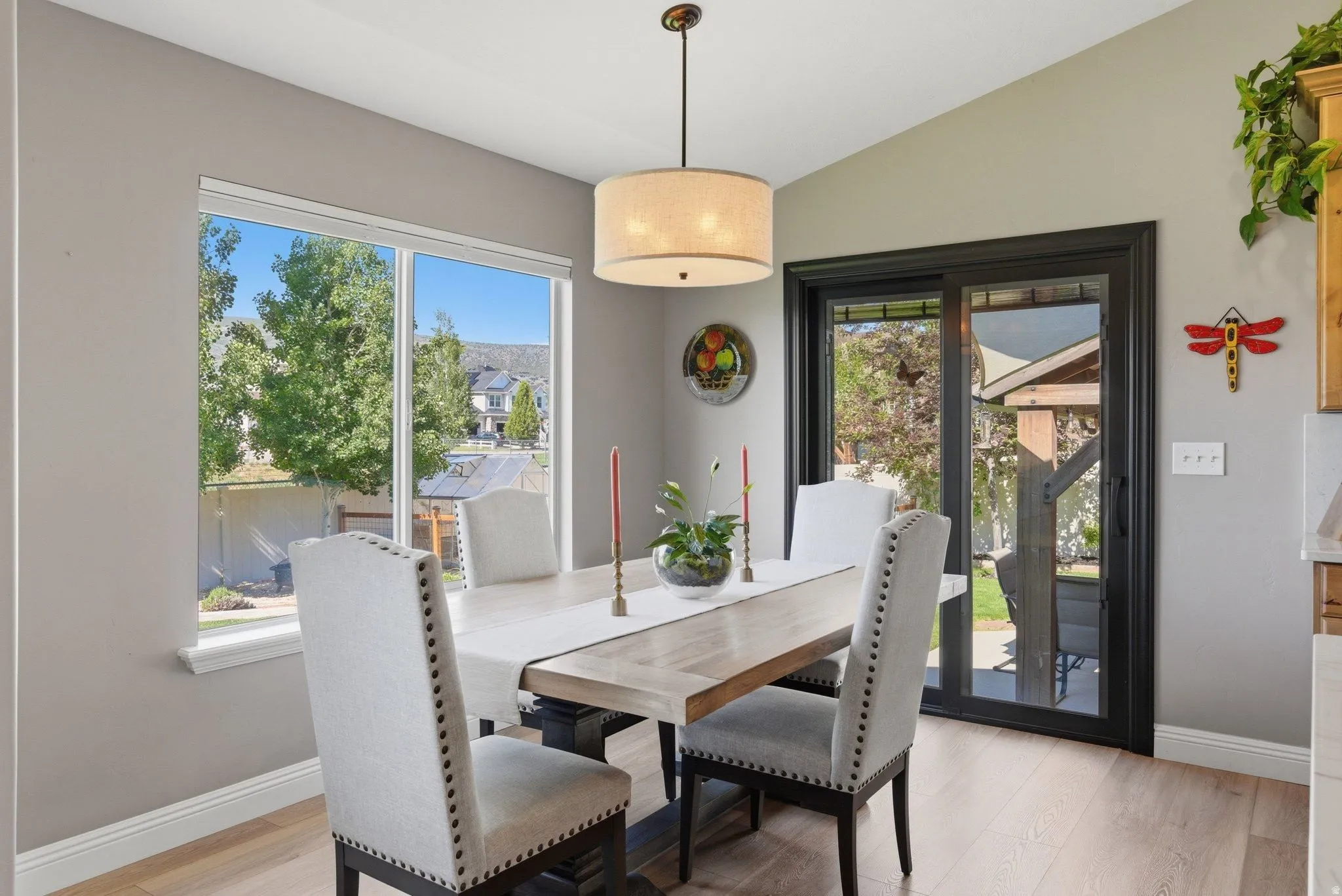 Dining area featuring wood-finish flooring, a contemporary drum pendant light, a large picture window, and a black-framed sliding glass door
