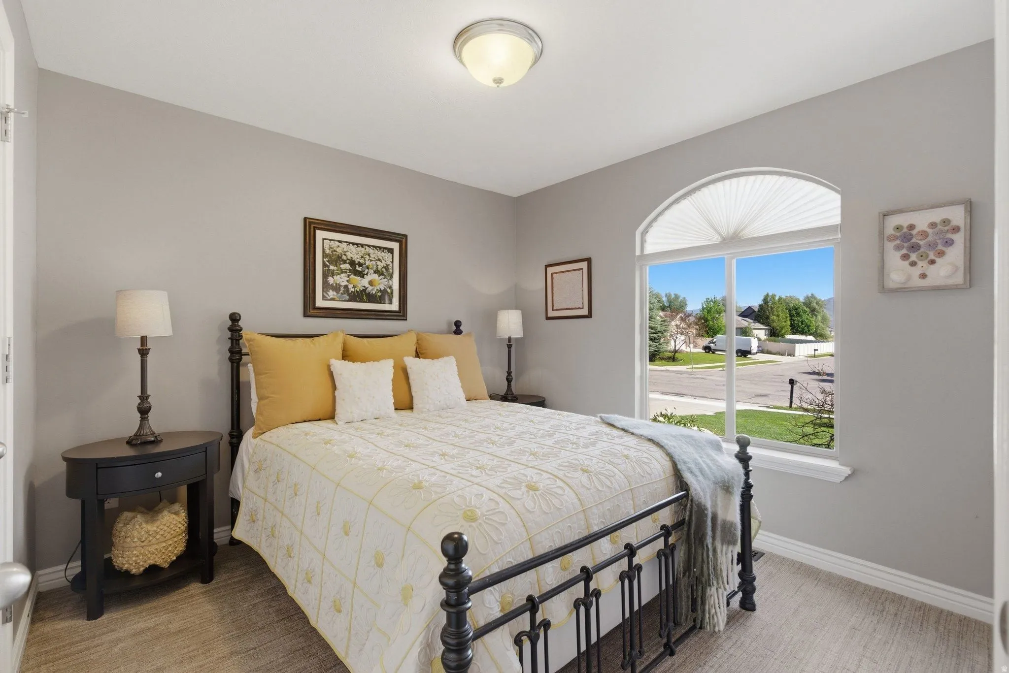 Bedroom featuring a large arched window with pleated shades, neutral wall paint, and soft carpet flooring