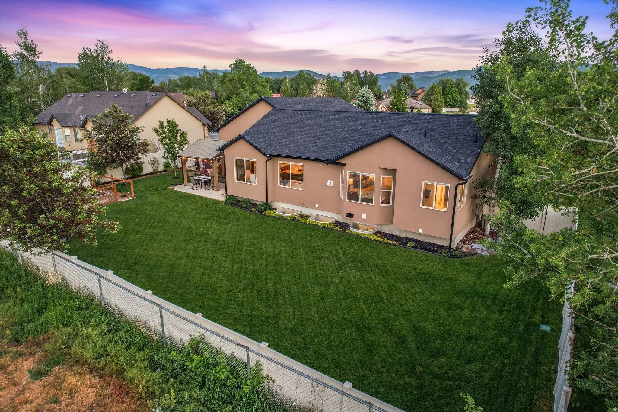 Expansive backyard featuring a manicured lawn, established trees, and a covered patio structure
