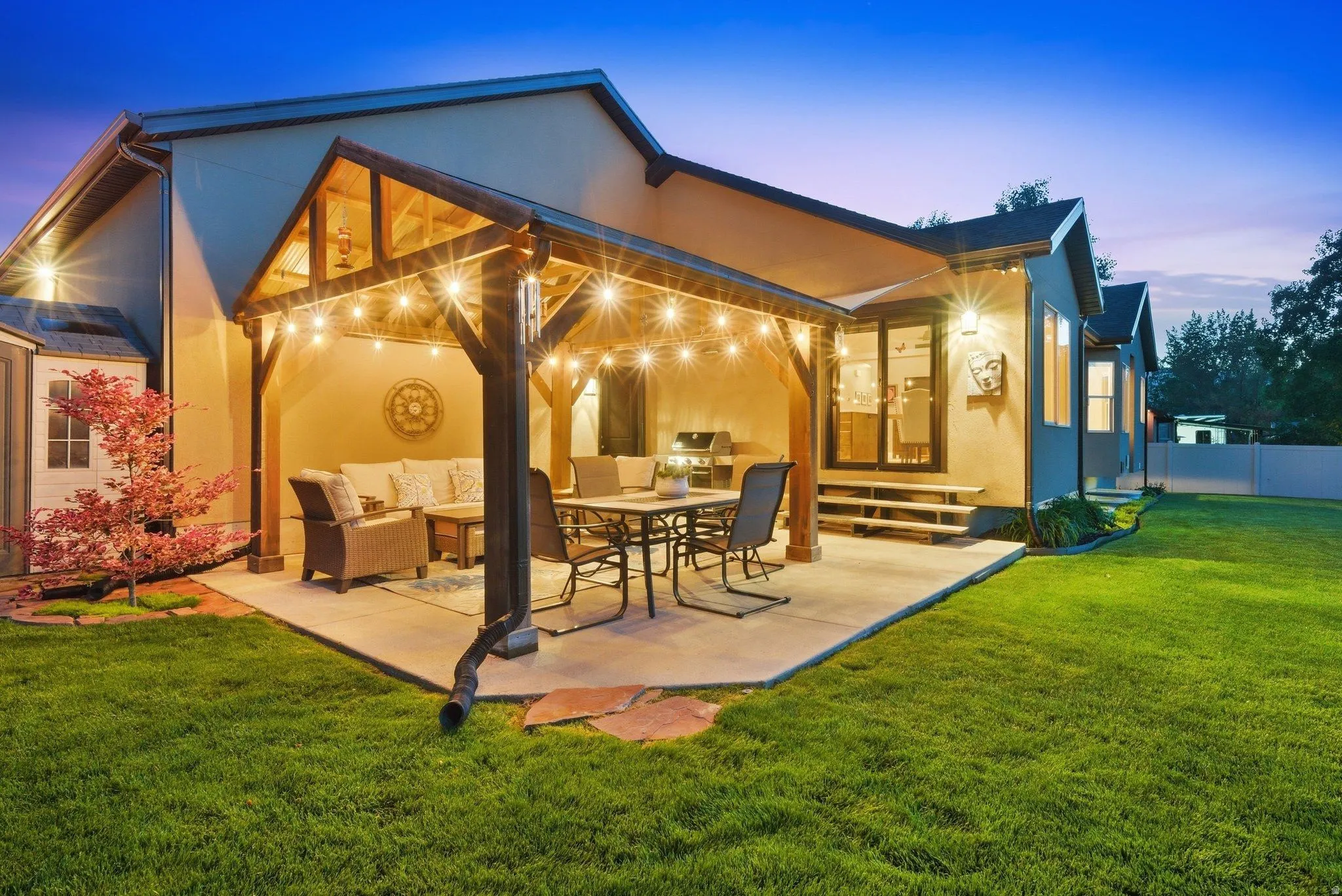 Rear exterior featuring a covered patio, concrete slab, built-in string lighting, and an expansive lawn