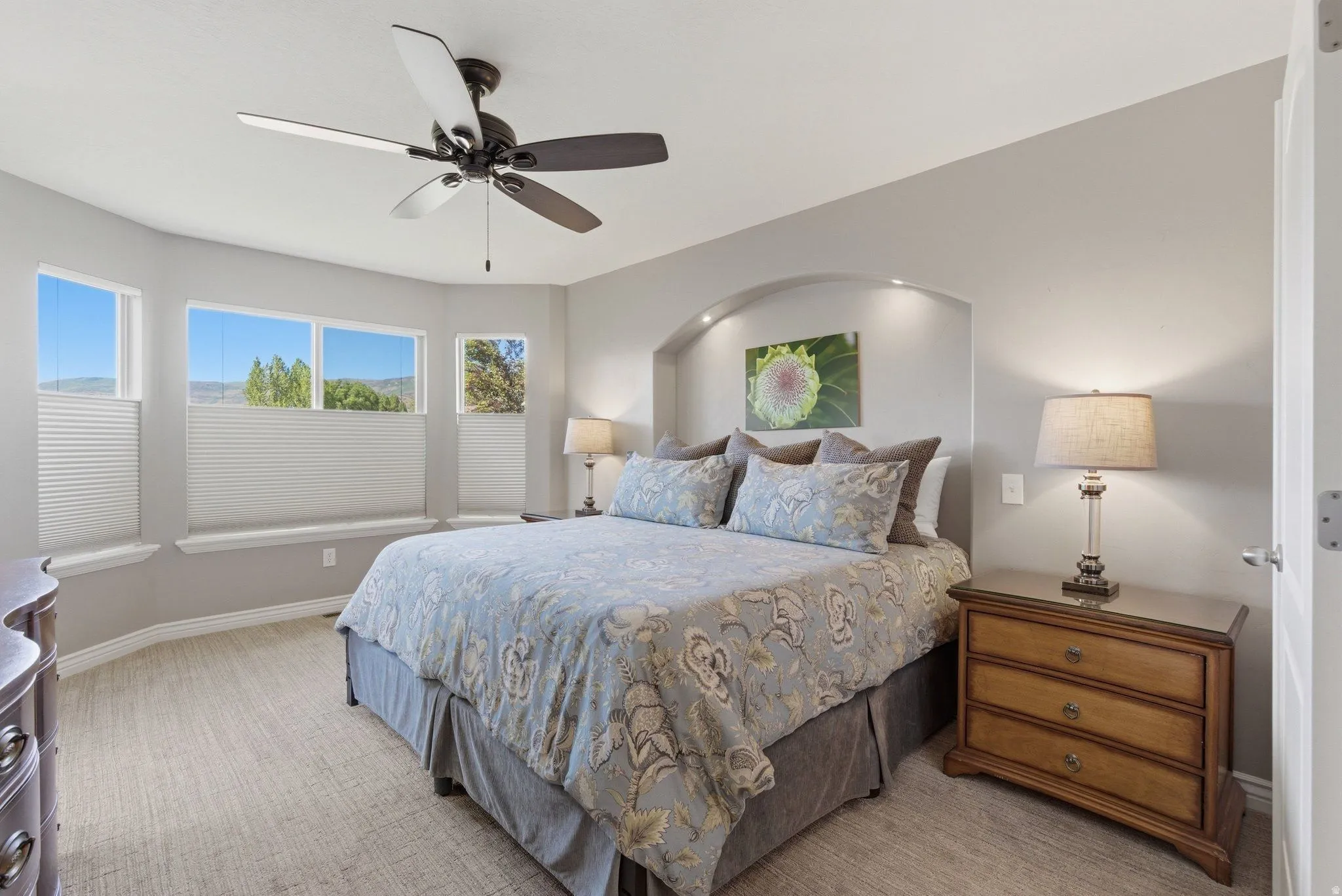 Bedroom featuring a bay window, ceiling fan with integrated lighting, recessed wall niche, and neutral carpeting
