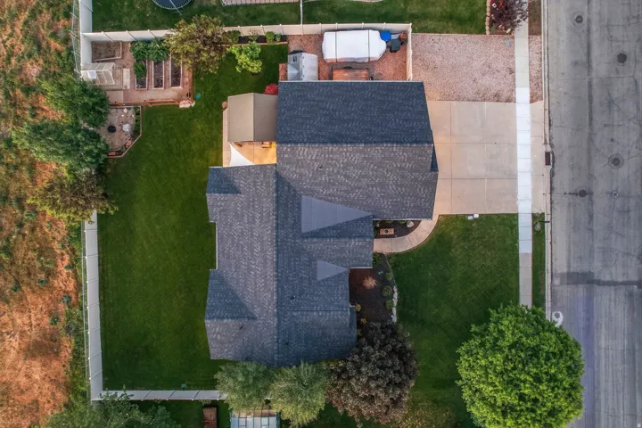 Aerial view of a residential property featuring a dark shingle roof, concrete driveway, and a manicured lawn