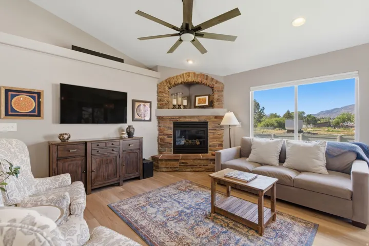 Living area featuring a floor-to-ceiling stone fireplace with an arched brick accent, light wood-finish flooring, and a vaulted ceiling with a ceiling fan