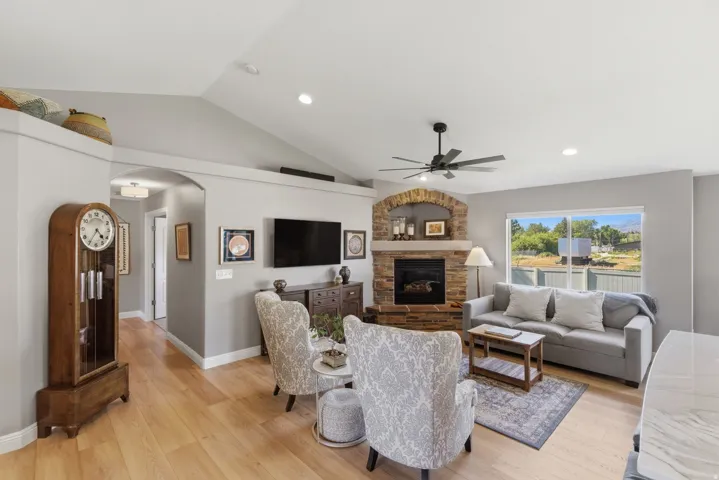 Spacious living area featuring a stone fireplace with a brick arch, light wood-finish flooring, recessed lighting, and a ceiling fan