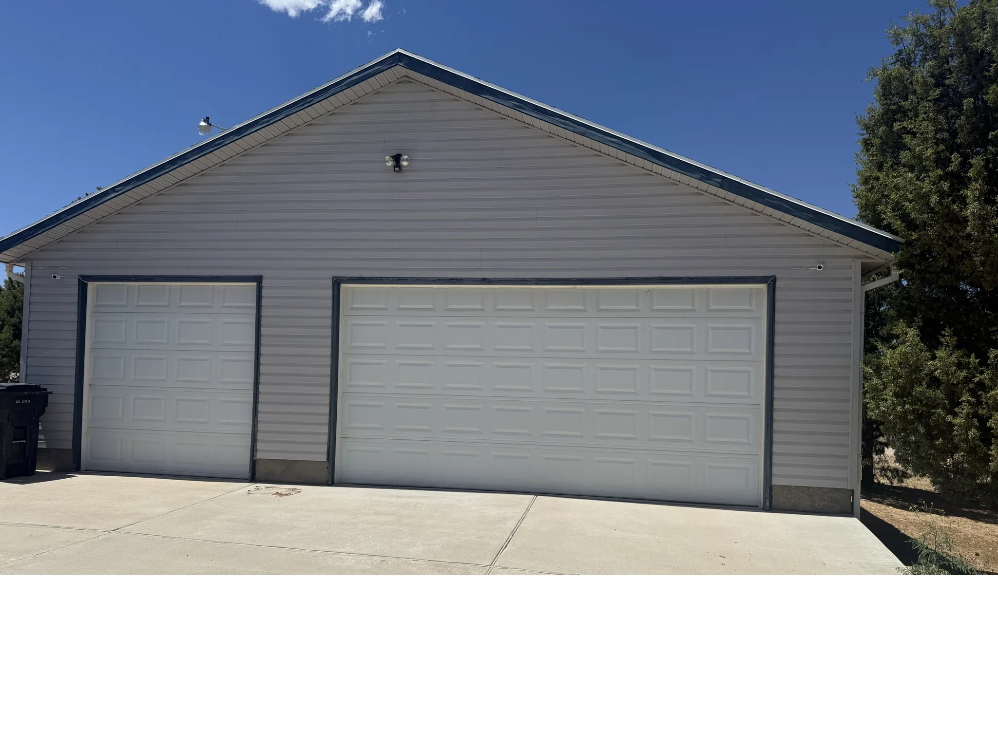 Garage featuring two white paneled doors, light grey horizontal siding, and a blue-trimmed gable roofline