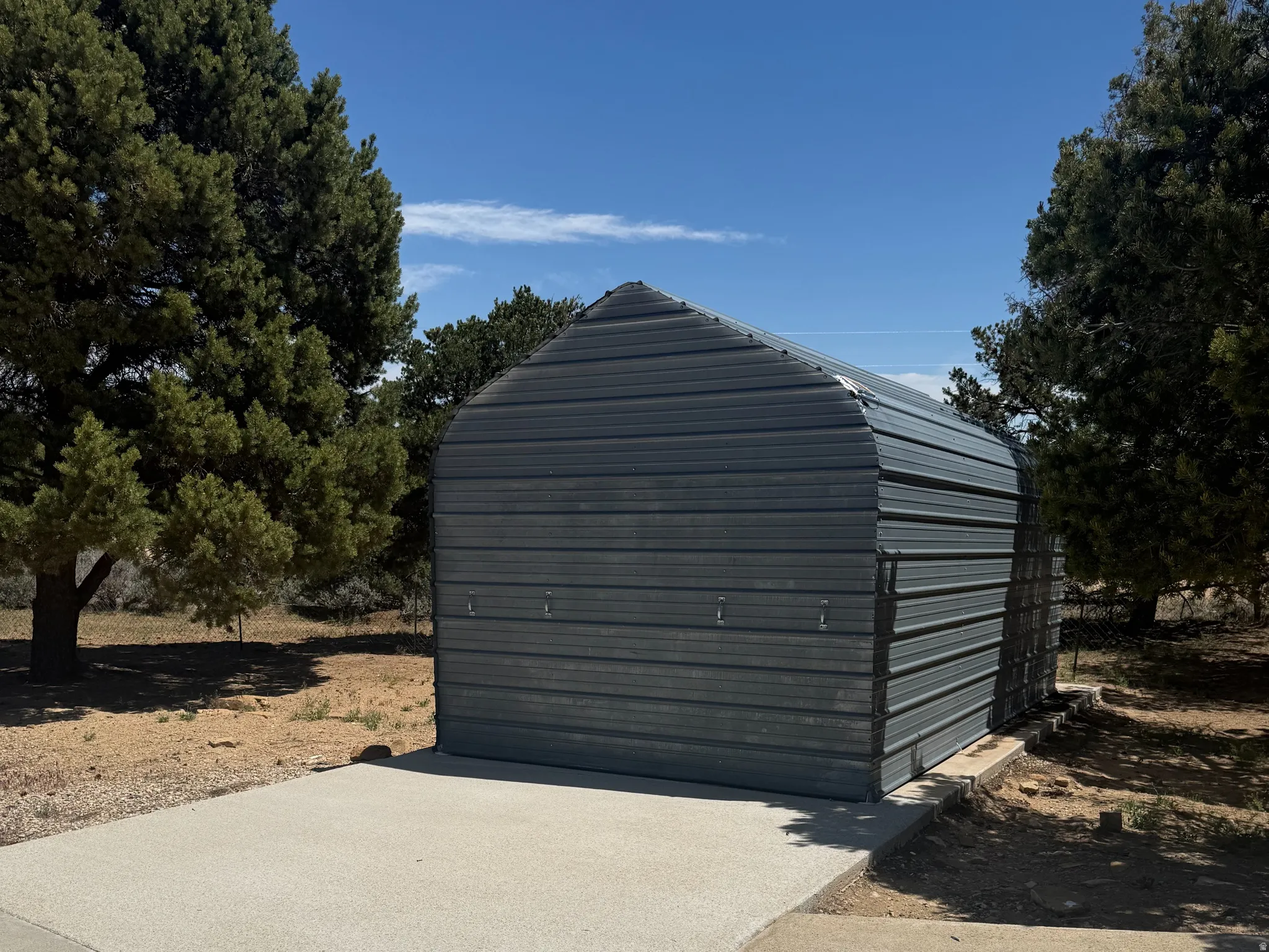 Corrugated metal BOAT storage structure with a rounded roofline, set on a concrete pad with a gravel perimeter