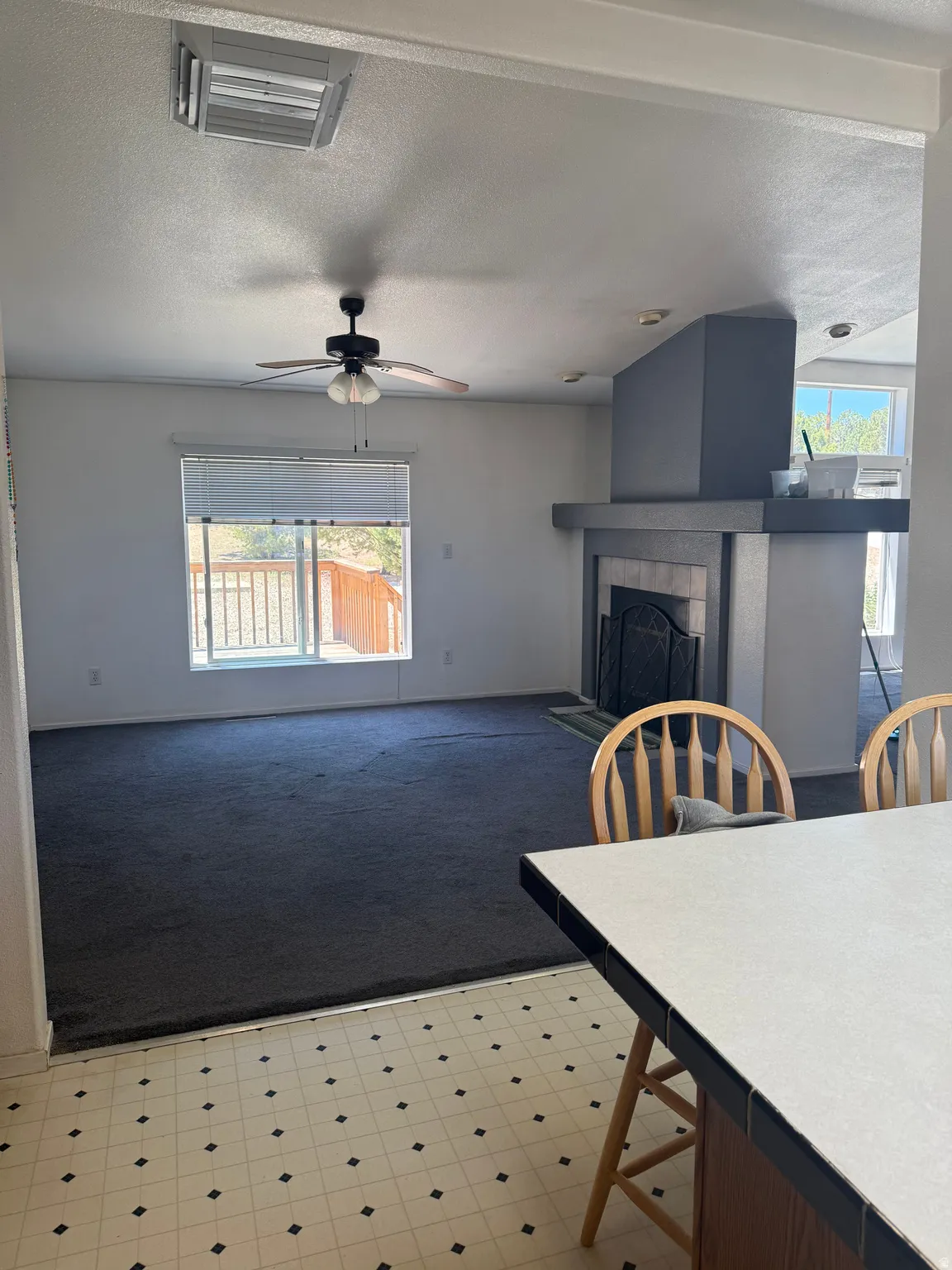 Open-concept living space featuring a ceiling fan, a large window, and dark carpeting