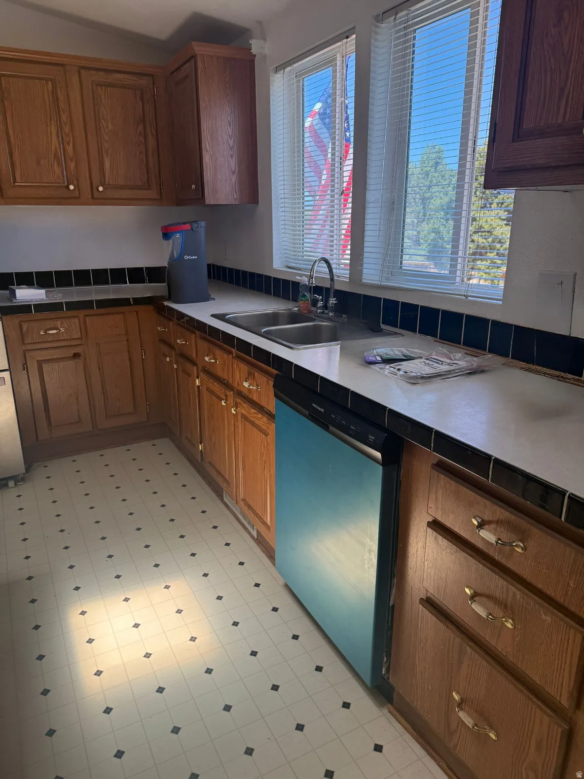 Kitchen featuring wood cabinetry, white countertops, dual basin stainless steel sink, and patterned floor tiles