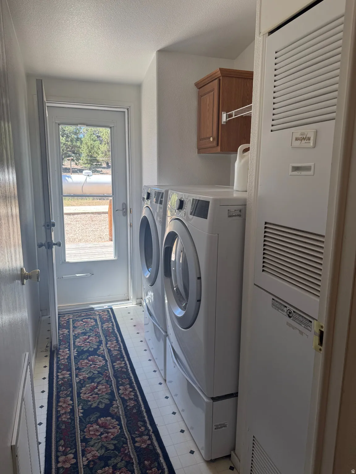 Dedicated laundry area featuring tile-patterned flooring, a white-framed glass paneled door, and an overhead storage cabinet