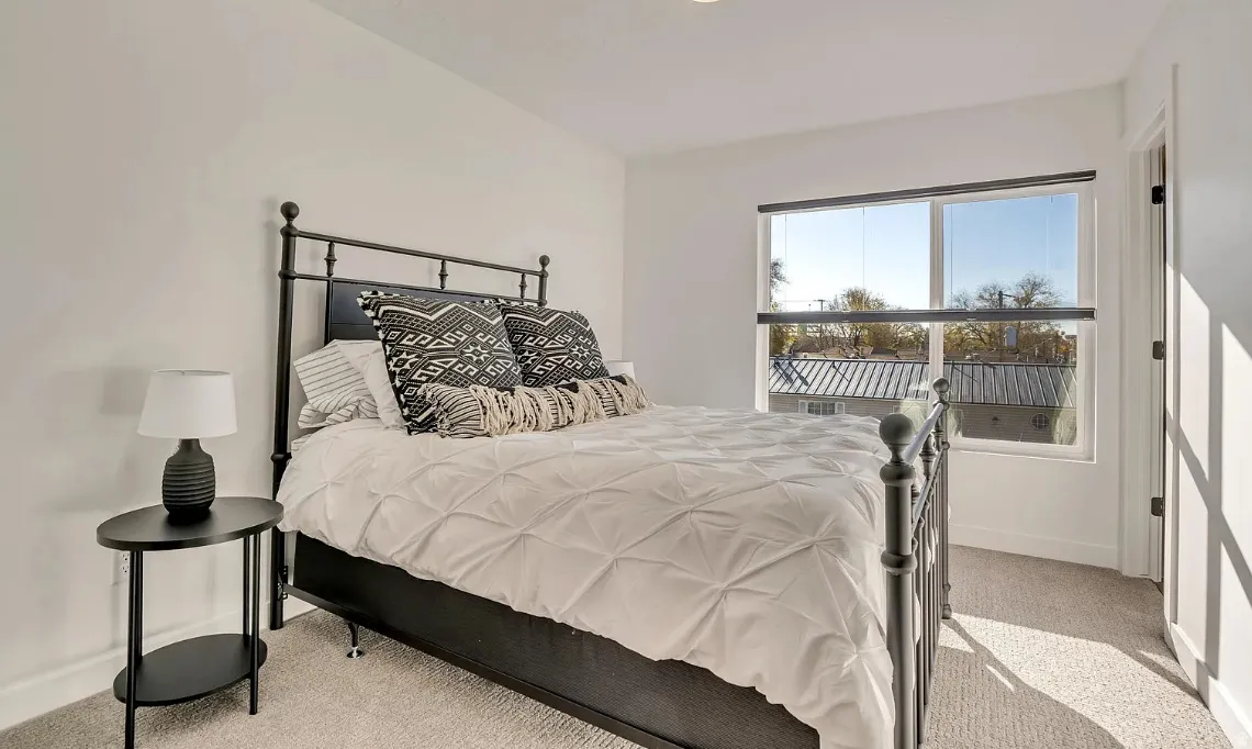 Bright interior space featuring a window with a roller shade, light-colored walls, and carpet flooring