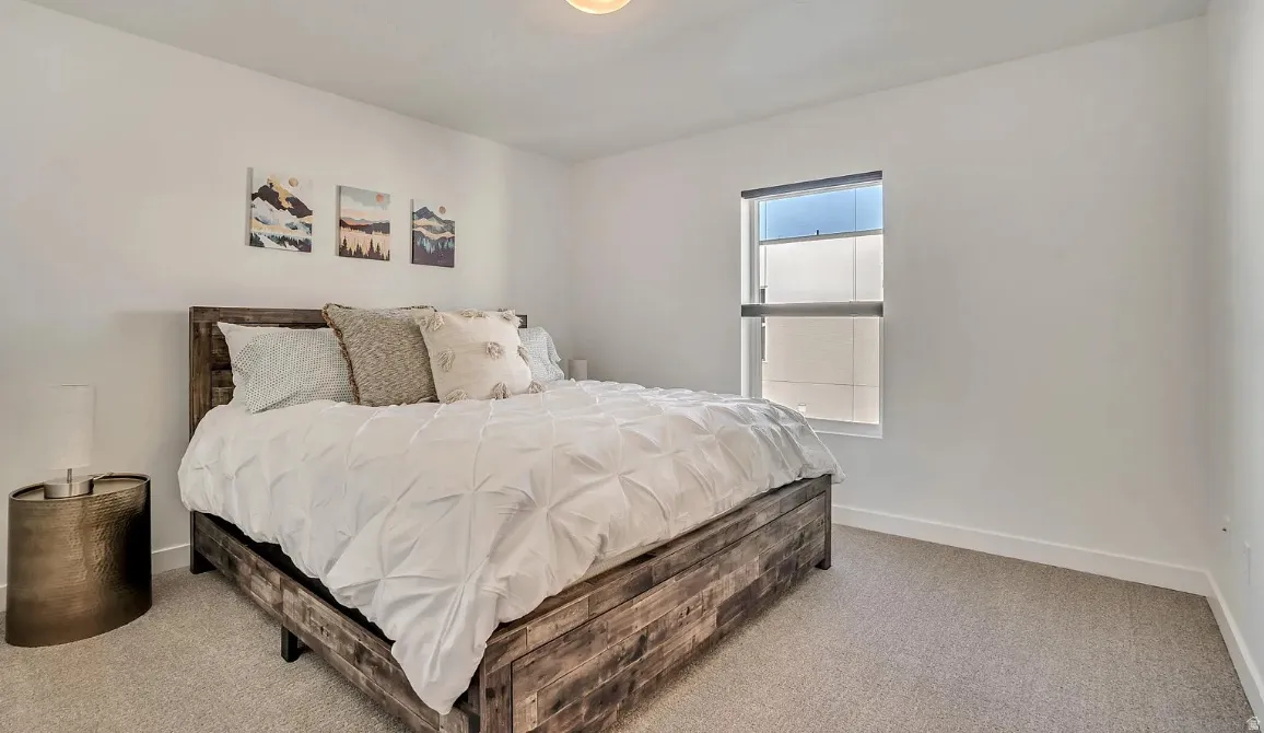 Spacious bedroom featuring light-toned carpeting, white walls, a single window with a roller shade, and a flush-mount ceiling light fixture
