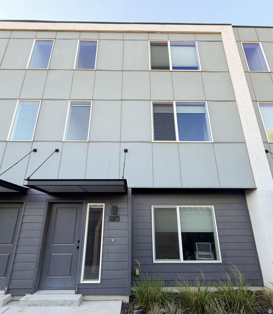 Contemporary multi-story exterior featuring a grey panel facade, dark grey horizontal siding, a modern entryway with a metal awning, and multiple windows