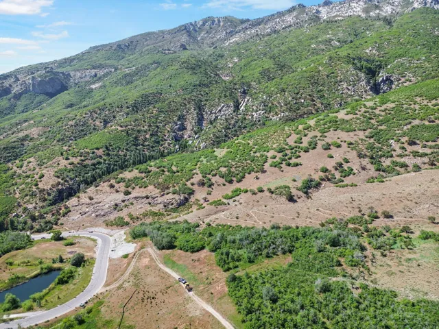 Expansive mountainous terrain with lush green vegetation, a winding paved road, and a tranquil pond