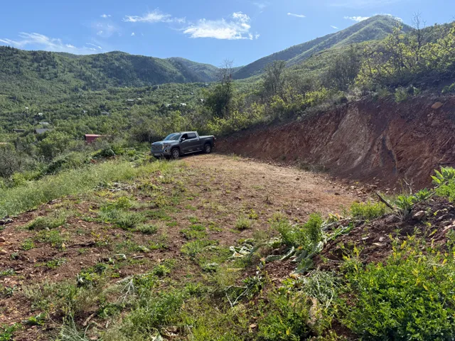 Mountainous terrain with natural vegetation, a partially graded lot, and visible distant structures