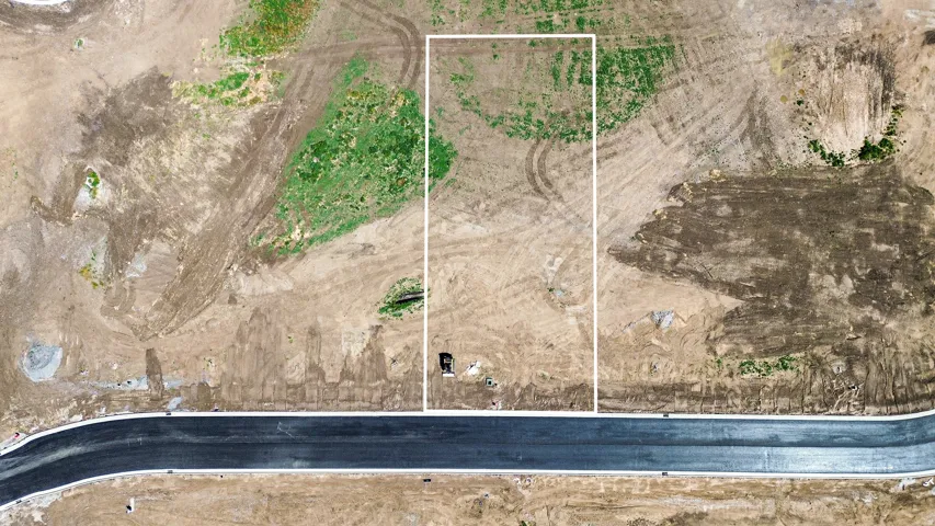 Developable land parcel featuring a paved road frontage, partially cleared terrain, and visible utility access points