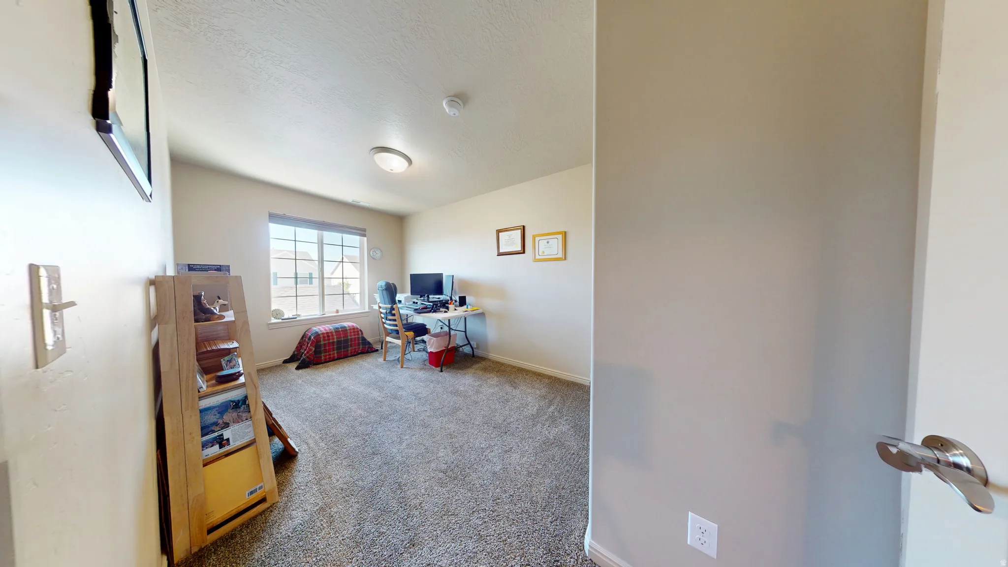 Carpeted room featuring a large window, neutral wall paint, a built-in ceiling light fixture, and a smoke detector