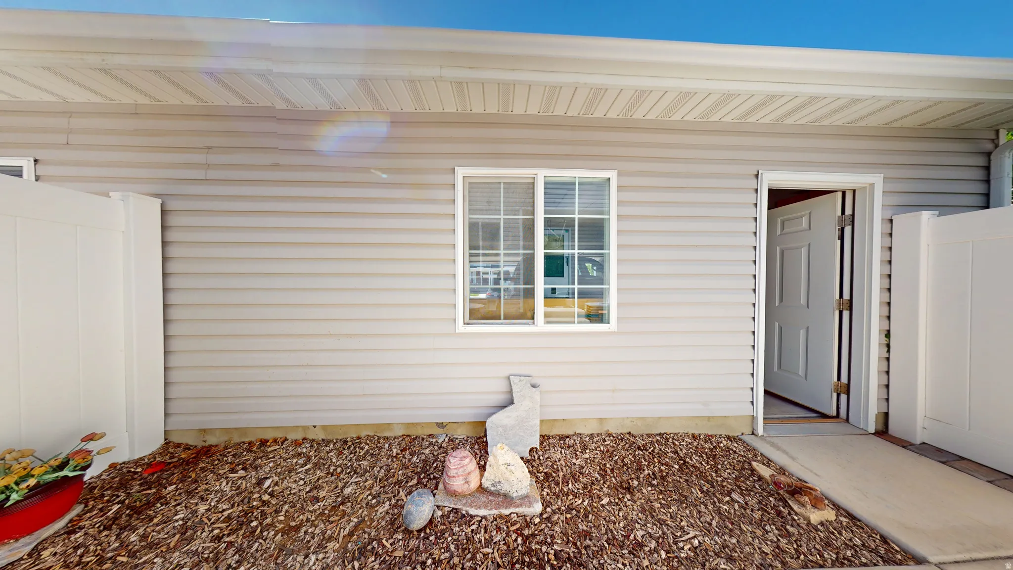 Exterior featuring horizontal siding, white trim windows, a white privacy fence, an entryway, and a ground covering of wood chips