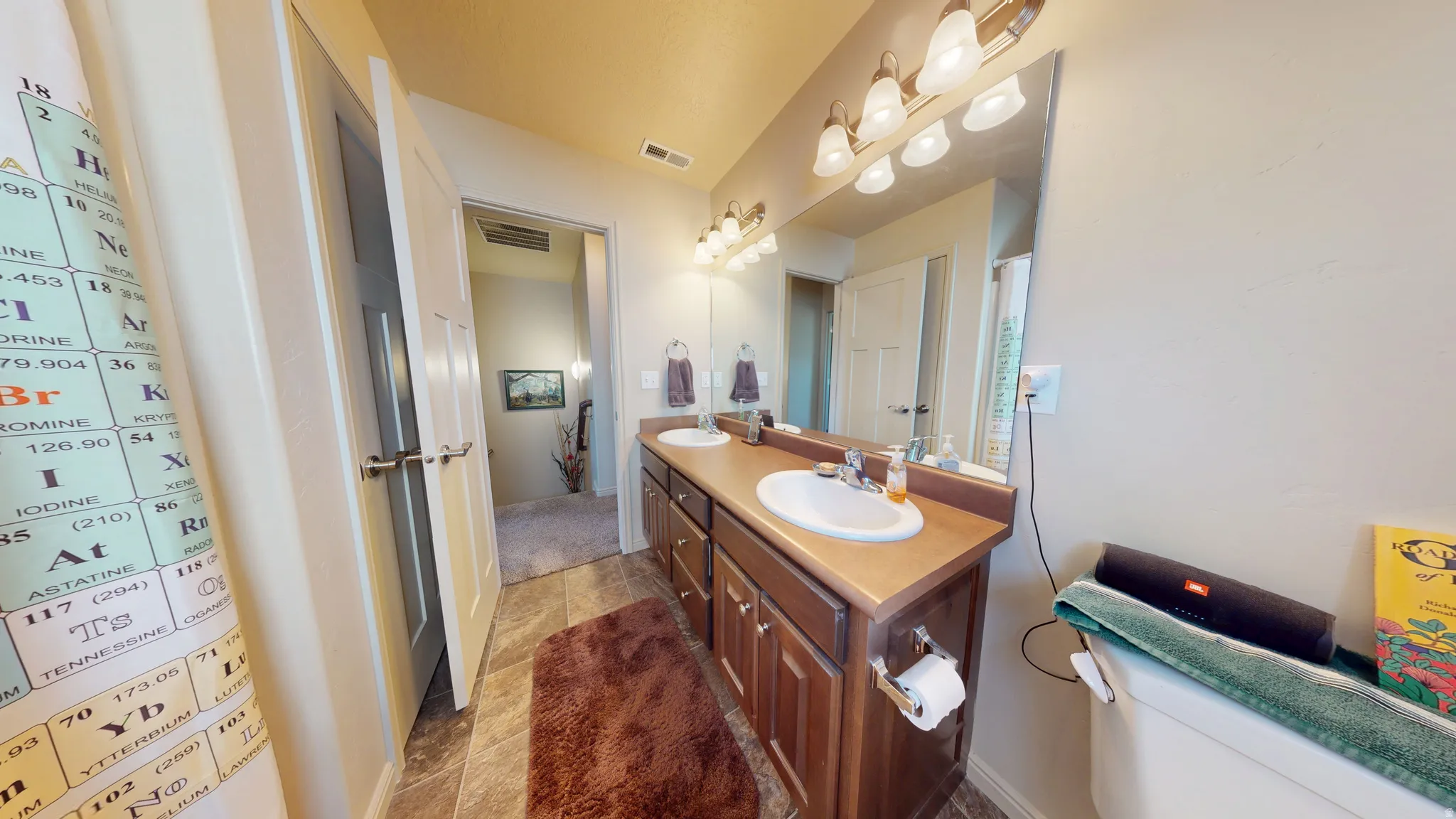 Bathroom featuring a dual vanity with undermount sinks, wood-finish cabinetry, a large wall-mounted mirror, and overhead vanity lighting