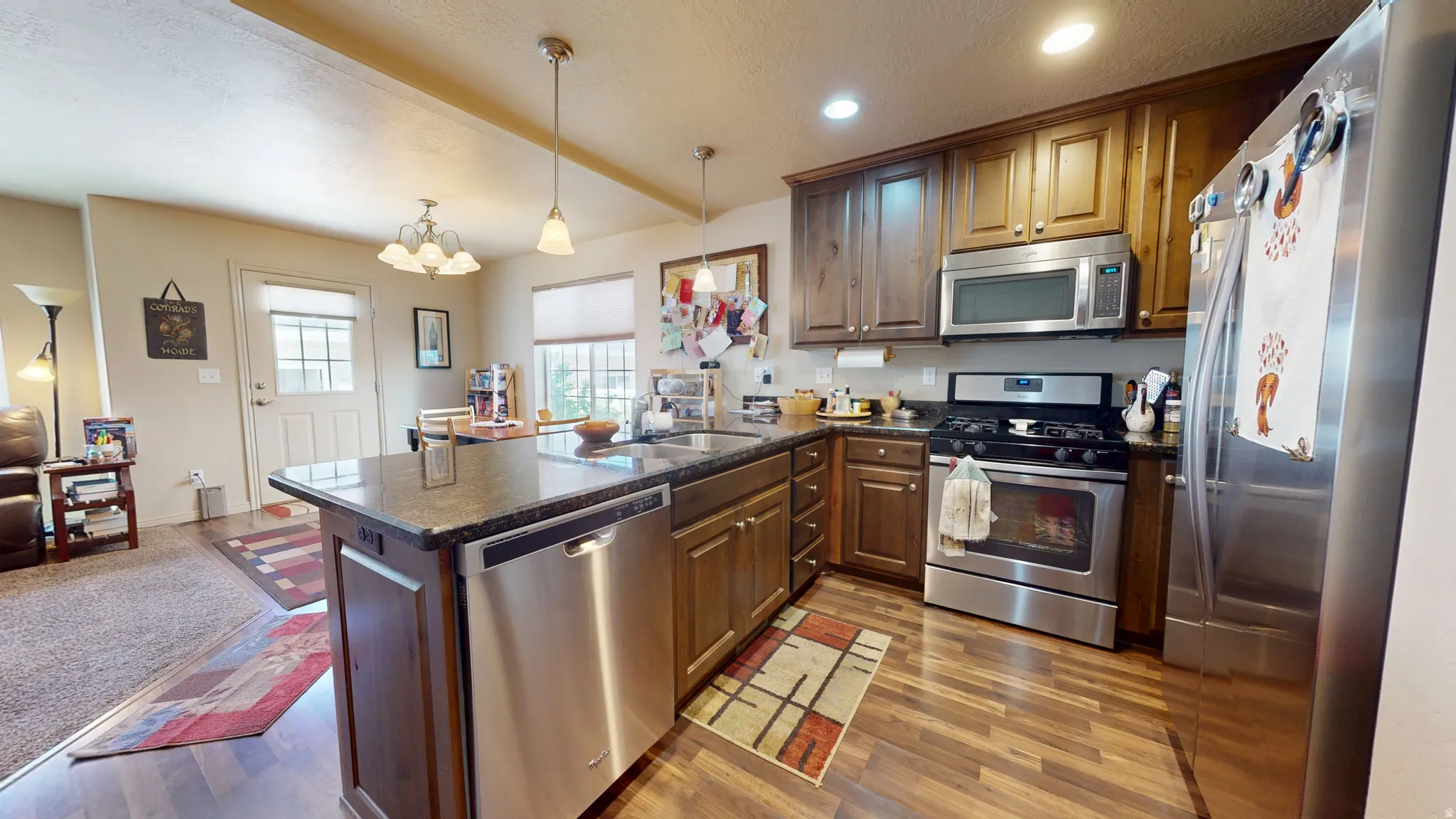 Kitchen featuring wood-finish flooring, dark stone countertops, wood cabinetry, and a full suite of stainless steel appliances