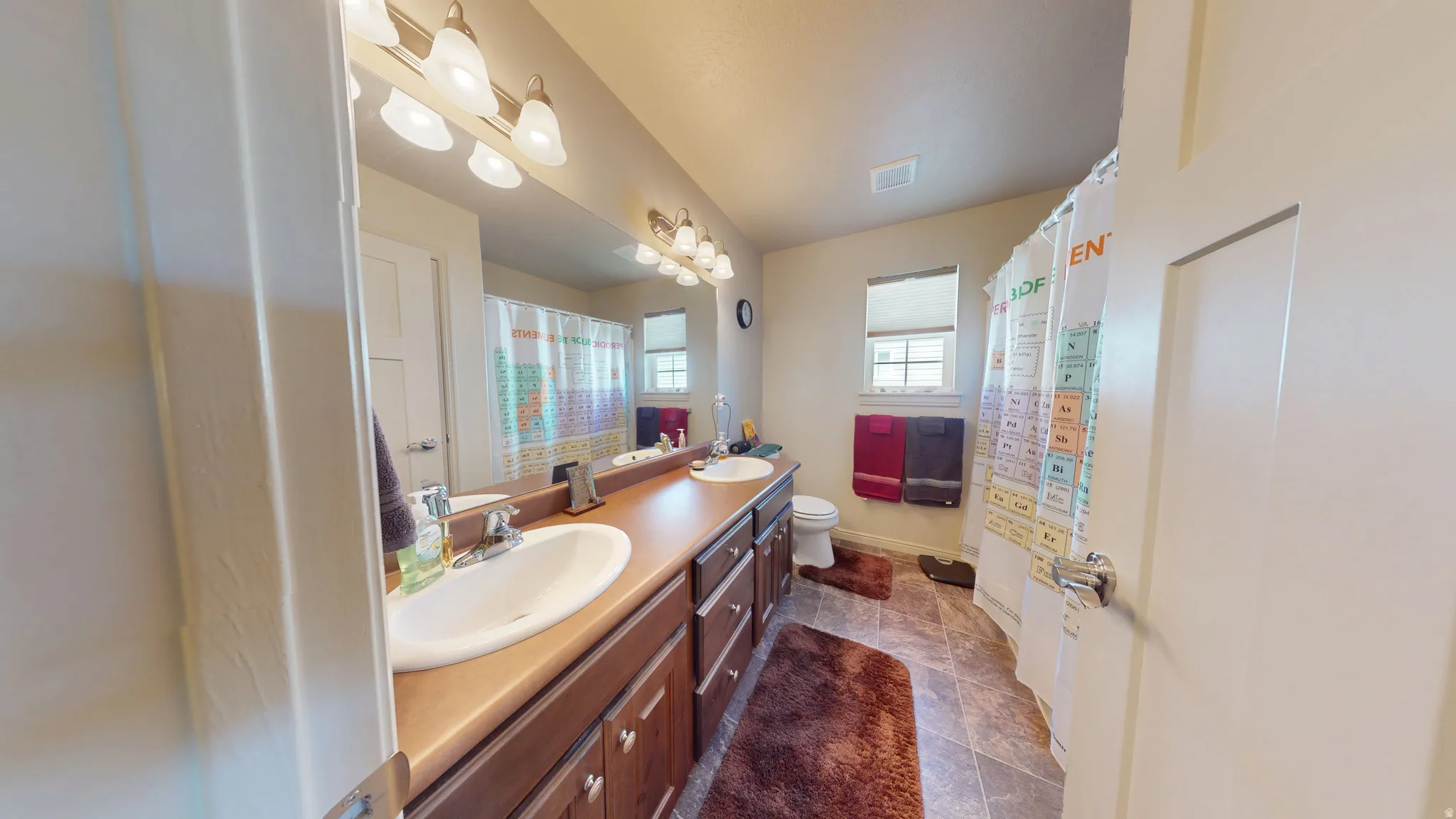 Bathroom featuring a dual vanity with integrated sinks, a lengthy countertop, and ample under-sink storage cabinetry