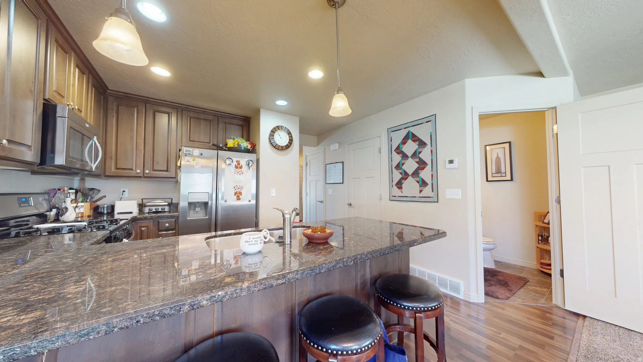 Kitchen featuring a granite countertop island with integrated sink, stainless steel appliances, recessed lighting, and wood-finish flooring