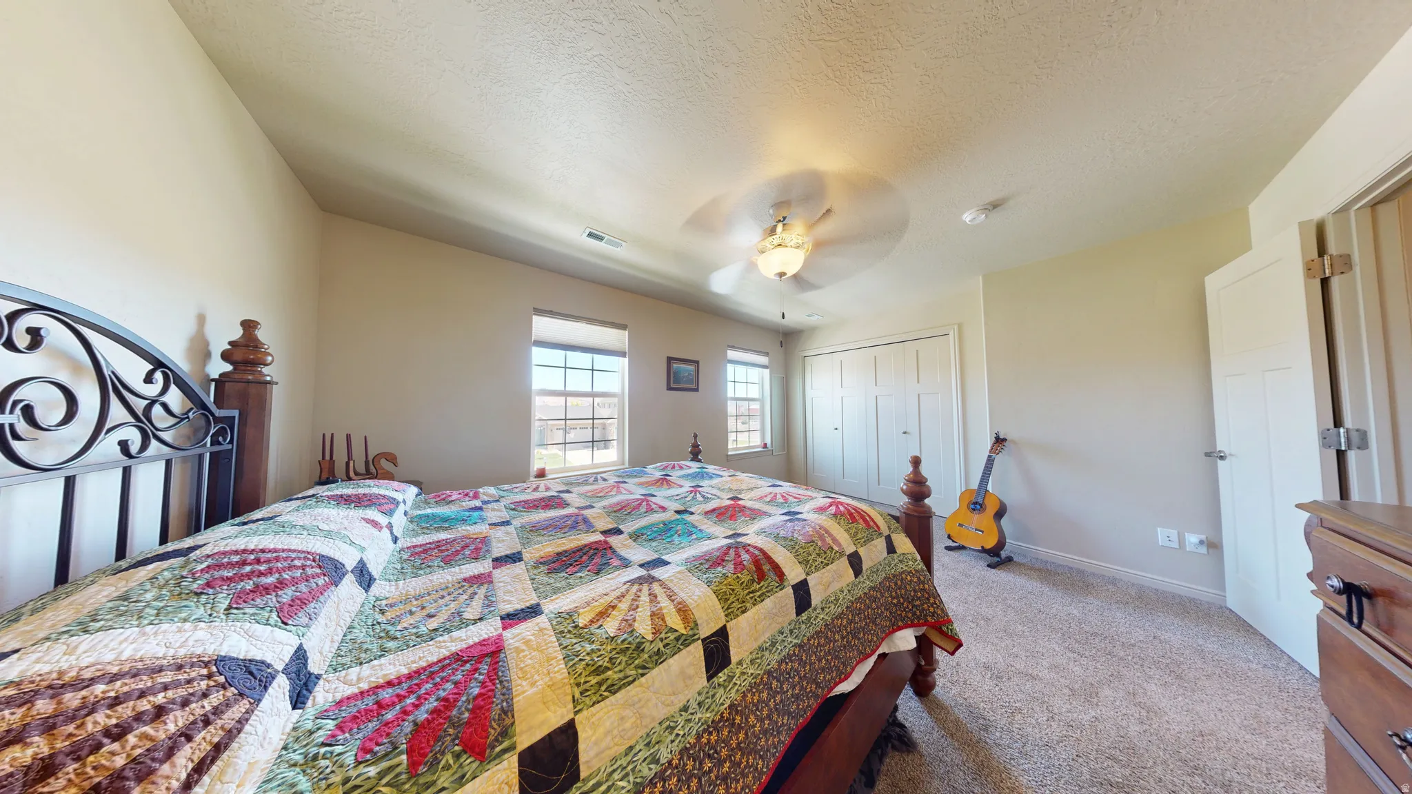 Carpeted bedroom featuring two windows, a ceiling fan with integrated lighting, and a closet with bi-fold doors