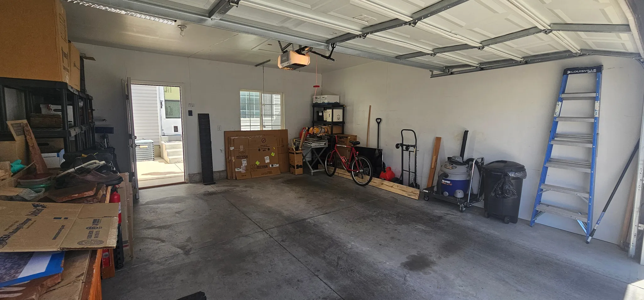 Spacious garage featuring a concrete floor, white walls, overhead garage door with opener, and an interior access door